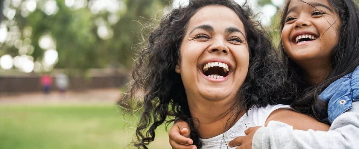 A laughing Latina mother carries her daughter on her shoulders